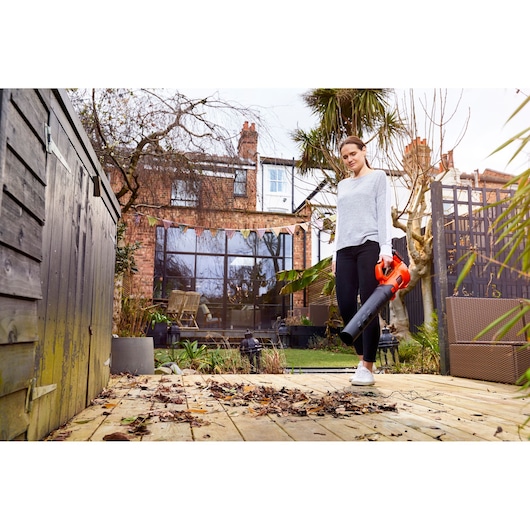 BLACKDECKER BCBL200B leaf blower held outdoors, clearing leaves from wooden patio, garden background.