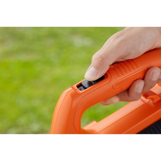 Close-up photo of a hand operating the BLACKDECKER BCBL200L40 leaf blower handle and power button outdoors.