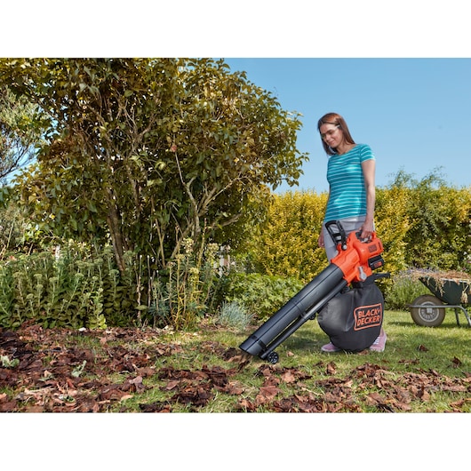 BLACK+DECKER BCBLV3625L1 leaf blower vacuum used in garden, orange and black, person collecting leaves.