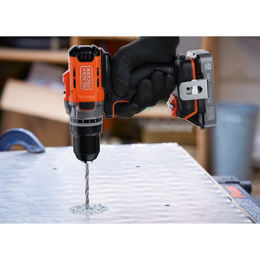 Photo of BLACK+DECKER BCD382D1 cordless drill in use, drilling into metal surface, close-up side view.