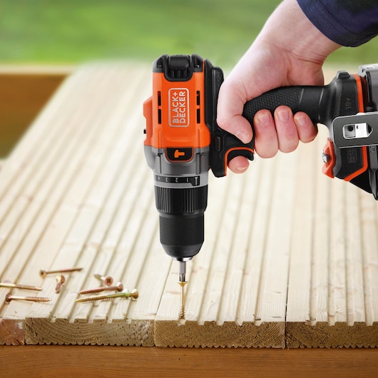 BLACK+DECKER BCD383D1 cordless drill driving a screw into wood, close-up with screws on surface.