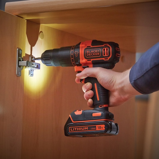 BLACK+DECKER BCD700HTSA cordless drill with lithium battery, used to install a hinge in wooden furniture.