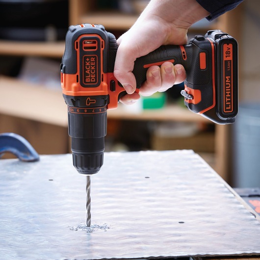 Photo of BLACK+DECKER BCD700S2AFC cordless drill with 18V lithium battery in use, drilling into a metal sheet.