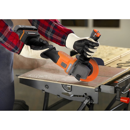 BLACKDECKER BCG6L8N cordless angle grinder in use, cutting tile on a workbench, close-up side view.