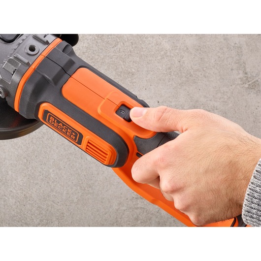 Close-up of a hand operating the power switch on a BLACK+DECKER BCG720N cordless angle grinder.