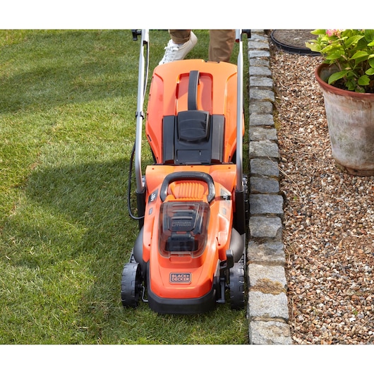 BLACKDECKER BCMW33184L2 cordless lawn mower in orange, top view on grass near stone border.