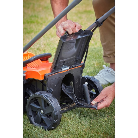Photo of BLACKDECKER BCMW33184L2 lawn mower rear compartment open, showing wheel and user adjusting cover on grass.