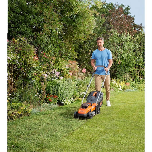 Photo of BLACKDECKER BCMW3336L1 lawn mower in use on a garden lawn, orange and black, outdoor setting.