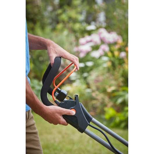 BLACKDECKER BCMW3336L1 lawn mower handle close-up, foam grip and orange safety bar in garden.
