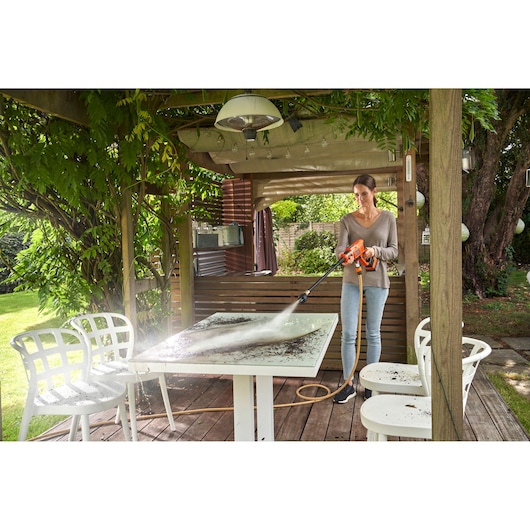 BLACKDECKER BCPC18D1 pressure washer cleaning a patio table outdoors under a wooden pergola.