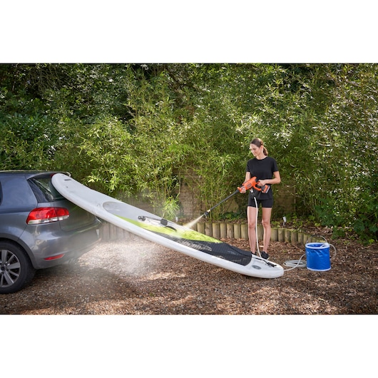 BLACKDECKER BCPC18D1 pressure washer cleaning a paddleboard beside a car outdoors.