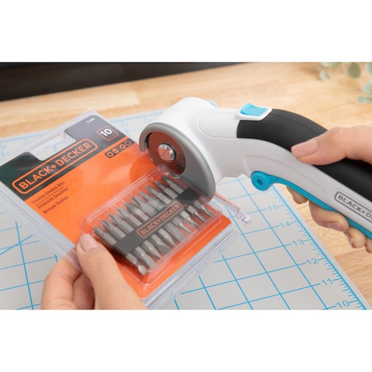 BLACKDECKER BCRC115 rotary cutter opening a BLACKDECKER drill bit package on a grid cutting mat.