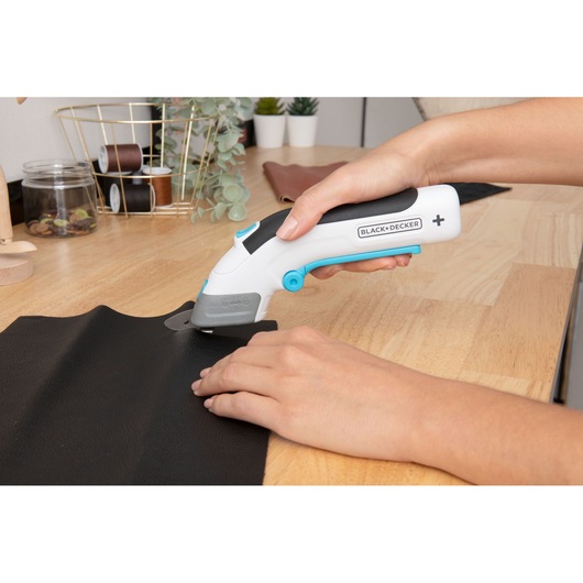 Photo of BLACK+DECKER BCSC115 electric fabric cutter in use cutting black material on a wooden table.