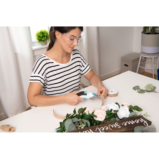 BLACKDECKER BCSC115 cordless glue gun used for crafting floral decorations at a white table, side angle