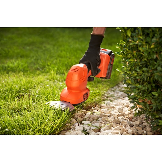 BLACKDECKER BCSS18B cordless grass shear trimming lawn edge near bushes and stones.