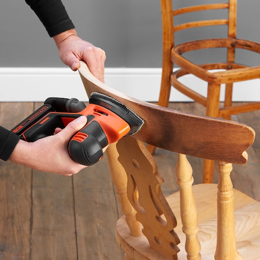 BLACKDECKER BDCDS18N cordless sander in use on wooden chair backrest, close-up angle.