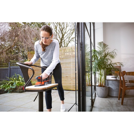 Photo of BLACKDECKER BDCDS18N sander being used on a chair outdoors near a patio door.