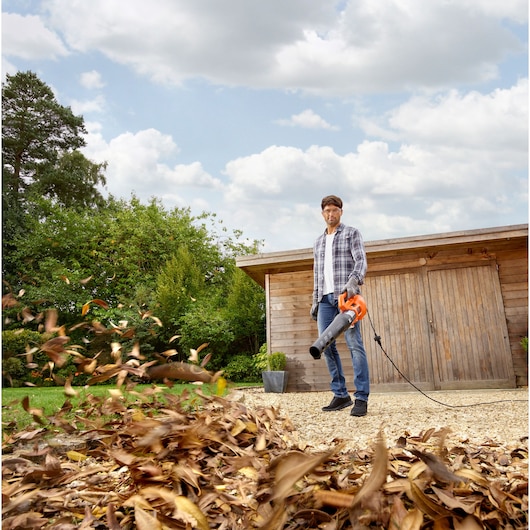 BLACKDECKER BEBL185 corded leaf blower used outdoors to clear leaves near wooden shed.
