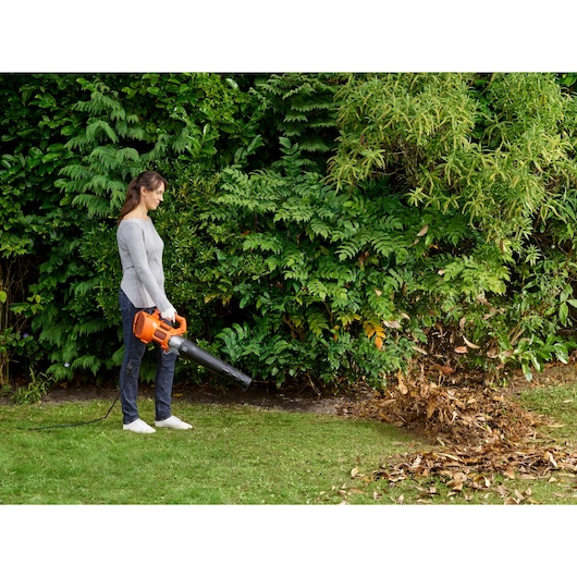 BLACKDECKER BEBL185 corded leaf blower in use outdoors, orange and black, clearing leaves from lawn.