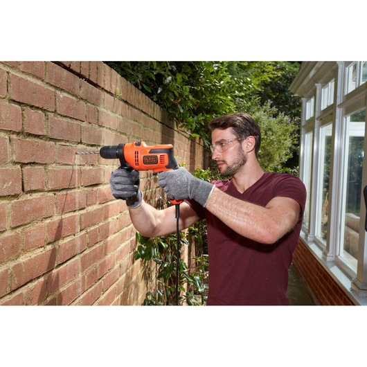 BLACK+DECKER BEH200 corded drill being used outdoors on a brick wall, user wearing gloves.