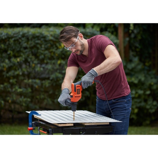 Photo of a person using a BLACKDECKER BEH200 corded drill on a workbench outdoors, drilling into a metal sheet.