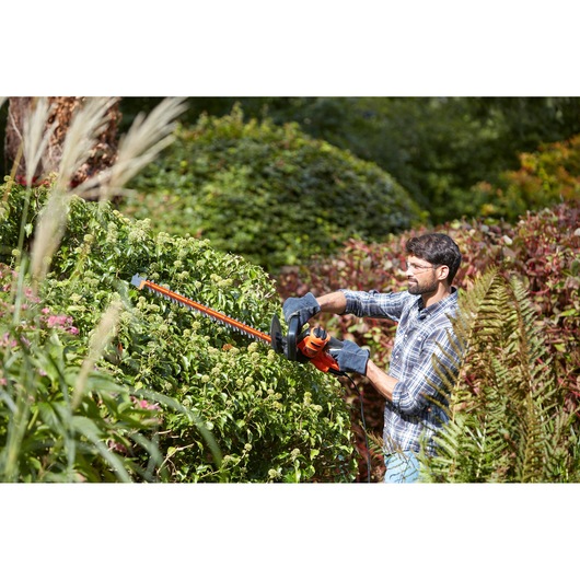 BLACKDECKER BEHTS501 hedge trimmer in use cutting green bushes outdoors.