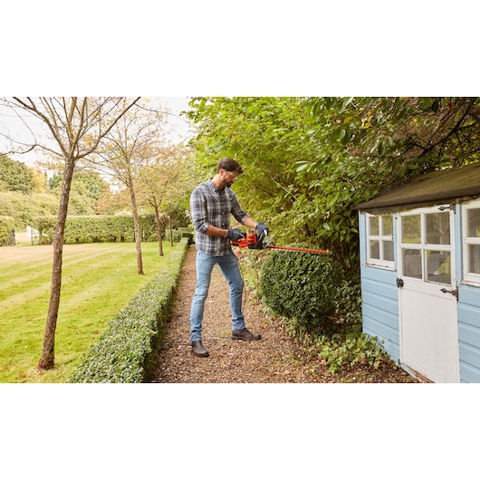 BLACKDECKER BEHTS501 hedge trimmer in use trimming garden bushes outdoors.