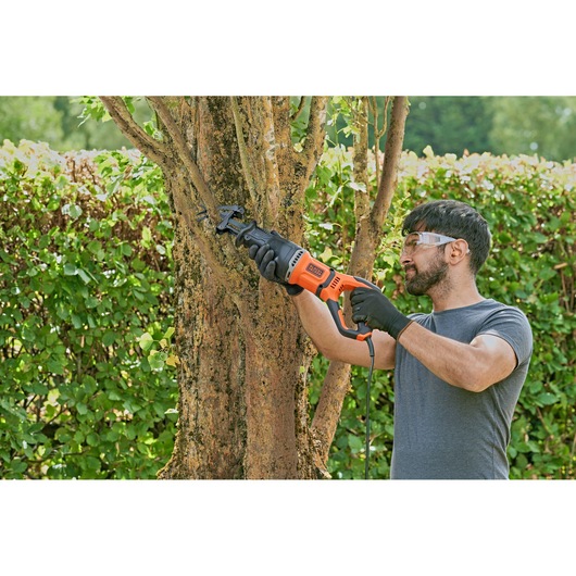Person using BLACK+DECKER BES301 reciprocating saw to cut a tree branch outdoors, wearing gloves.