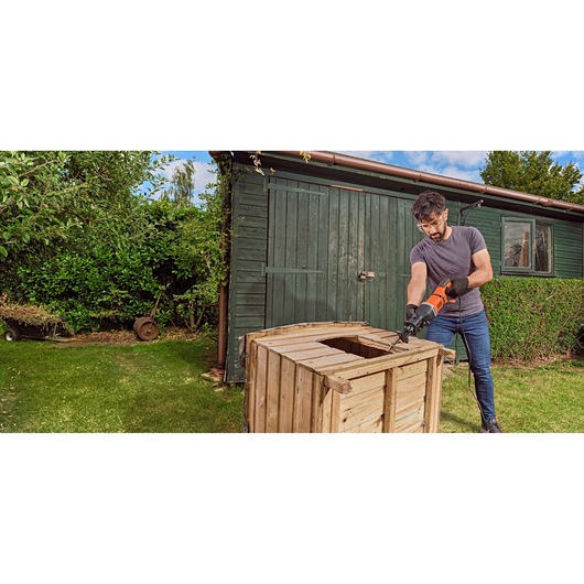 Man using BLACK+DECKER BES301 reciprocating saw to cut wood outdoors next to a green shed.