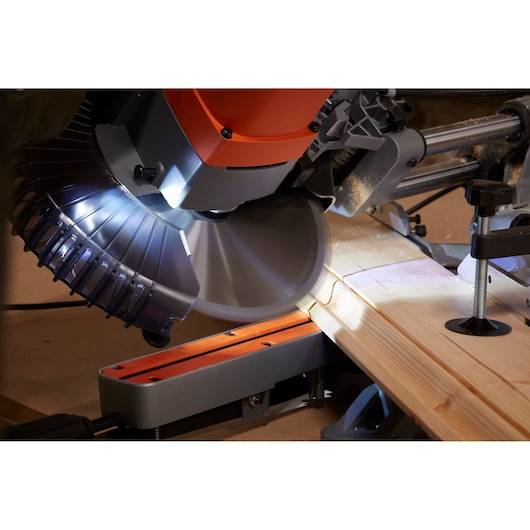 BLACKDECKER BES710 miter saw cutting light wood, close-up angle, showing illuminated blade and cutting action.