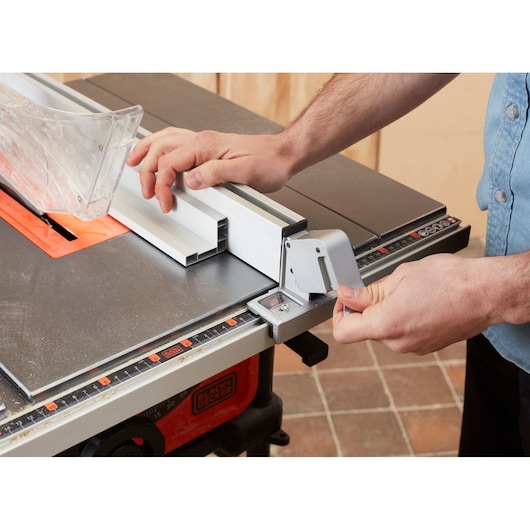 Photo of BLACKDECKER BES720 table saw in use, showing hands adjusting the fence and clear blade guard, side angle.