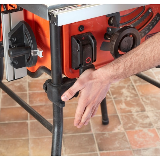 Photo of a BLACKDECKER BES720 table saw detail, showing a hand adjusting the stand on a tiled floor.