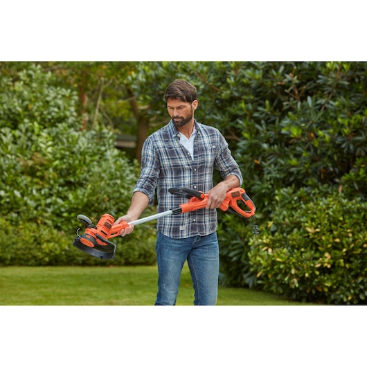 Person using BLACK+DECKER BESTA528 orange electric grass trimmer in garden.