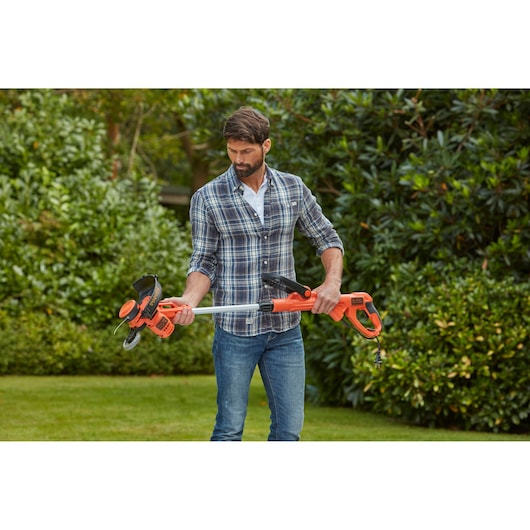 Photo of BLACKDECKER BESTA528 orange electric grass trimmer held outdoors by a person in casual clothing.
