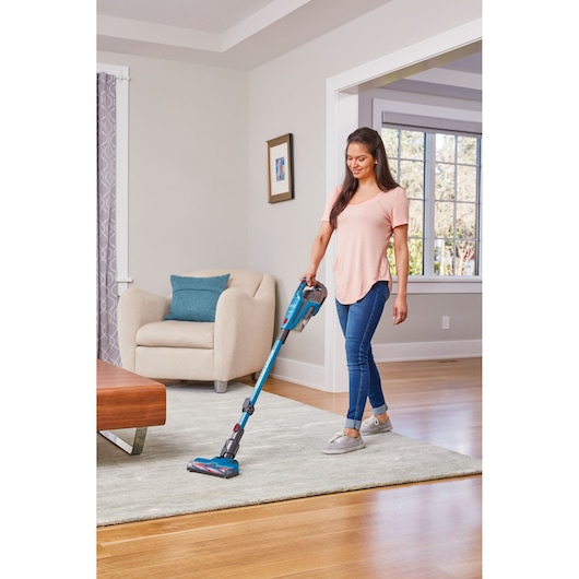 BLACKDECKER BHFE520J cordless stick vacuum cleaner in use on a light-colored rug in a modern living room.