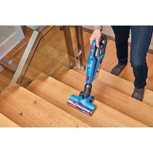 BLACKDECKER BHFE520J cordless stick vacuum cleaning wooden stairs, blue body and red accents.