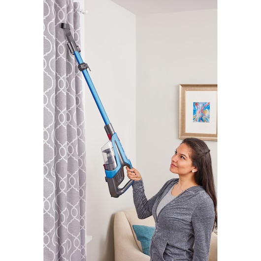BLACKDECKER BHFE520J stick vacuum cleaner cleaning curtains in a living room setting.