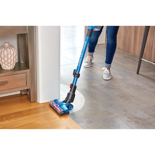BLACKDECKER BHFE520J cordless stick vacuum cleaning near corner, blue handle, close-up, indoor flooring.