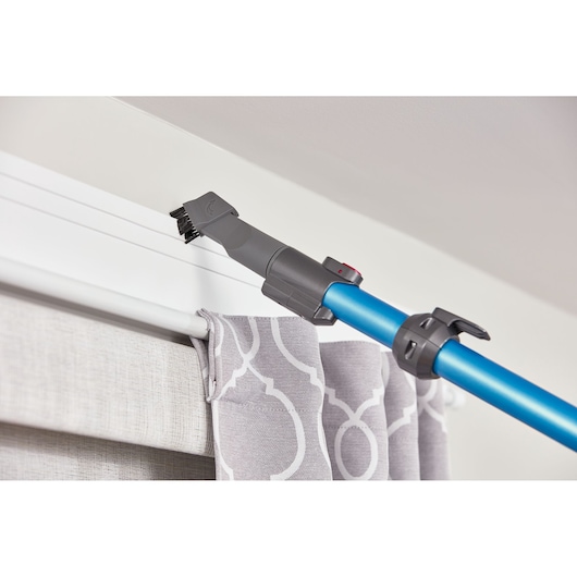 BLACKDECKER BHFE520J cordless vacuum with brush attachment cleaning above a curtain on a white wall, close-up.