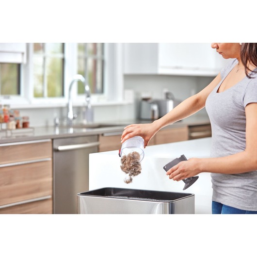 Photo of person emptying dirt from BLACKDECKER BHFE520J vacuum container into a kitchen trash bin.