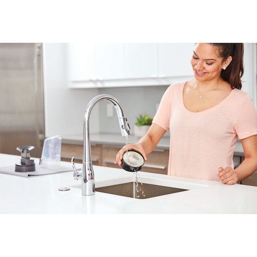 Photo of person rinsing BLACKDECKER BHFE520J vacuum filter under kitchen faucet in modern kitchen.
