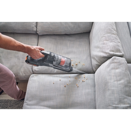 BLACK+DECKER BHFEA18D1 handheld vacuum cleaning crumbs from grey sofa upholstery.
