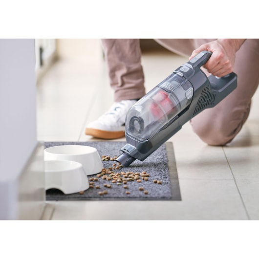 BLACKDECKER BHFEA515JB handheld vacuum cleaning pet food from mat near white bowls.