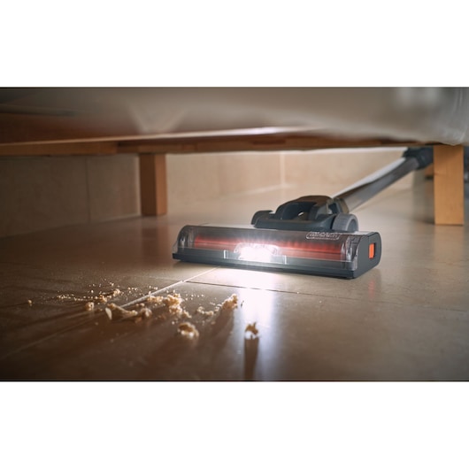 BLACKDECKER BHFEA515JB cordless stick vacuum with LED light cleaning debris under furniture, floor view.