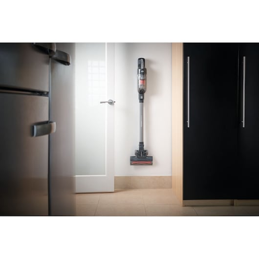 Photo of BLACKDECKER BHFEA515JB cordless stick vacuum stored upright against a white wall in a modern kitchen.