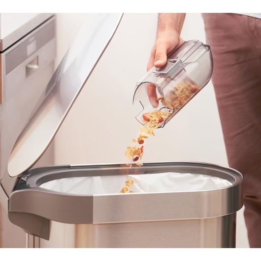 BLACKDECKER BHFEA515JB vacuum dust container being emptied into a stainless steel trash bin, side angle.
