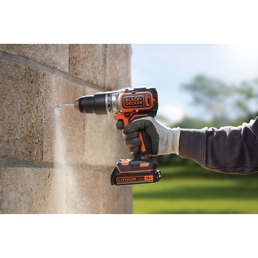 Photo of BLACK+DECKER BL188N cordless drill in use, drilling into a concrete wall outdoors.