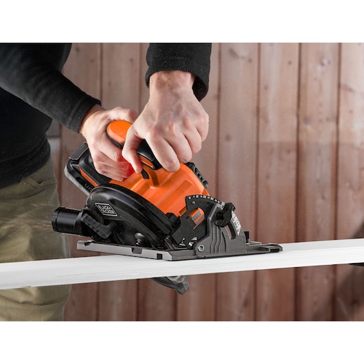 Photo of BLACKDECKER BLCCS78N circular saw in use, cutting a white board, hands gripping the orange handle.