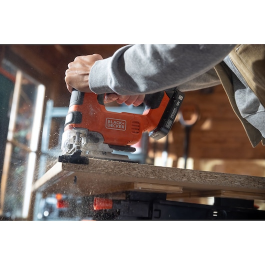 Photo of BLACK+DECKER BLCJS78N jigsaw cutting wood, handheld, visible sawdust, indoor workspace.