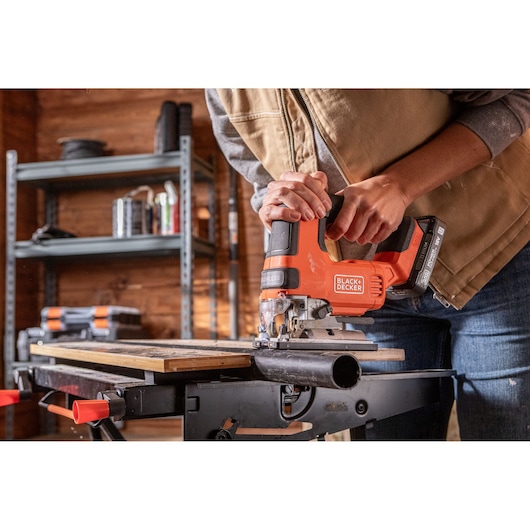 Photo of BLACK+DECKER BLCJS78N cordless jigsaw in use, cutting wood on a workbench in a workshop.